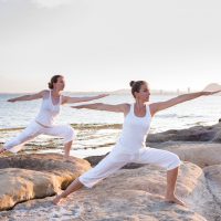 Two sisters are doing yoga exercises at the seashore of Mediterranean sea
